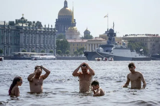 People swim in the Neva River on the beach of the Saint Peter and Paul Fortress in St. Petersburg, Russia, Wednesday, July 14, 2021, with the Winter Palace, the St.Isaac's Cathedral and a warship moored for incoming Navy Day celebration in the background. The temperature in St. Petersburg is 33C (91F). (Photo by Dmitri Lovetsky/AP Photo)
