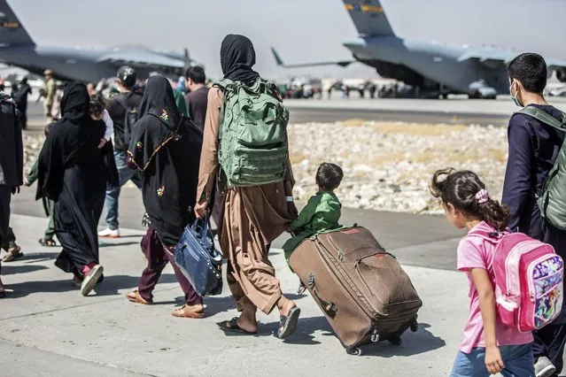 In this image provided by the U.S. Marine Corps, families walk towards their flight during ongoing evacuations at Hamid Karzai International Airport, Kabul, Afghanistan, Tuesday, August 24, 2021. (Photo by Sgt. Samuel Ruiz/U.S. Marine Corps via AP Photo)