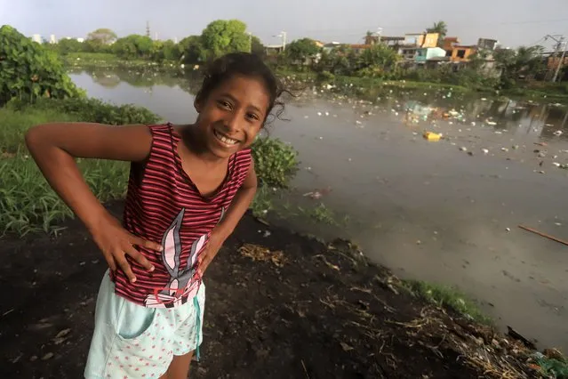 A girl smiles while eyeing the camera as she stands alongside the Sao Joaquim canal, its banks and water littered with garbage, in the Barreiro neighborhood of Belem, Brazil, Wednesday, August 9, 2023. According to the Instituto Trata Brasil, specializing in research of basic sanitation and water protection, the city of Belem, host of the Amazon Summit, has one of the worst sanitation rates in Brazil, with a sewage system available to only 17.1 % of the population. (Photo by Paulo Santos/AP Photo)