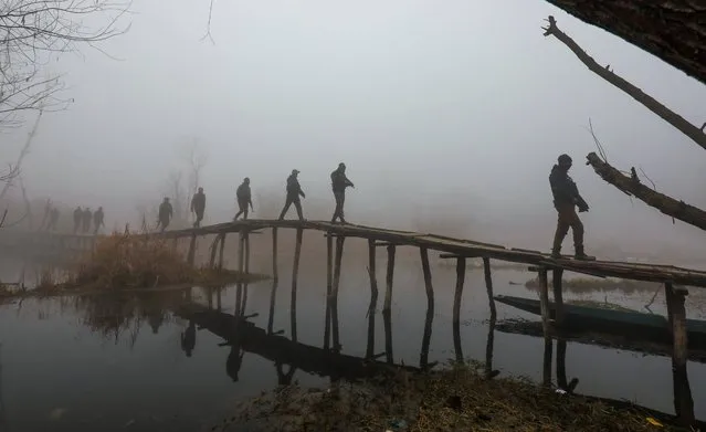 Indian policemen patrol on a wooden bridge on a cold and foggy day in Srinagar, Kashmir, India, 26 December 2023. The local weather department issued a forecast predicting prevailing weather conditions will continue until 31 December in the Himalayan region. Due to dense fog, there was slow traffic movement on major highways and roads in the region. Some morning flights at Srinagar International Airport were delayed due to low visibility. (Photo by Farooq Khan/EPA/EFE)