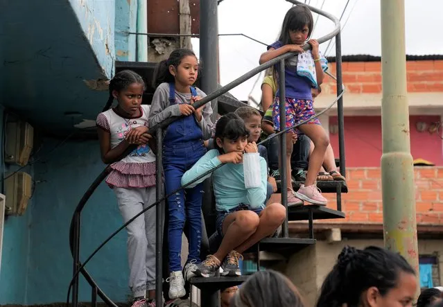 Girls watch an event for children at a soup kitchen in the Antimano neighborhood of Caracas, Venezuela, Tuesday, July 27,2021. The soup kitchen was celebrating a belated national children's day with different cultural activities, amid the new coronavirus pandemic. (Photo by Ariana Cubillos/AP Photo)
