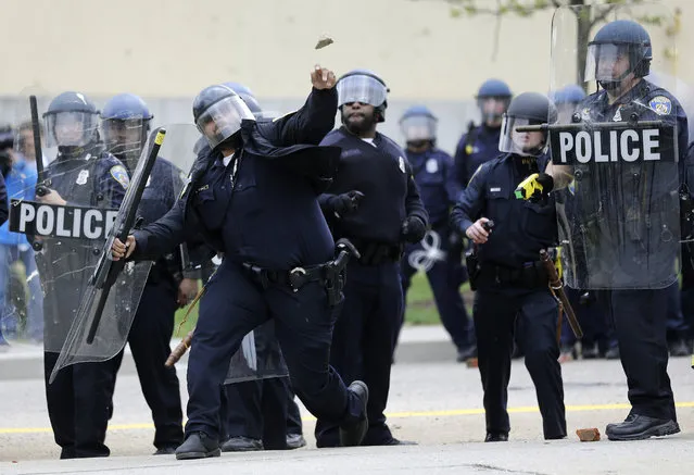 A police officer throws an object at protestors, Monday, April 27, 2015, following the funeral of Freddie Gray in Baltimore. (Photo by Patrick Semansky/AP Photo)