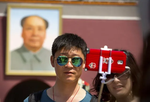 A tourist uses a selfie stick to take a photo of themselves in front of a large portrait of late Chinese leader Mao Zedong on the Gate of Heavenly Peace near Tiananmen Square in Beijing, Sunday, May 3, 2015. (Photo by Mark Schiefelbein/AP Photo)