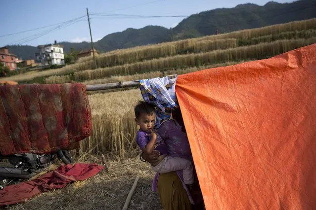 A Nepalese woman carries a child and stands beside a makeshift tent in Nalinchowk, near Kathmandu, Nepal, Thursday, May 14, 2015. (Photo by Bernat Amangue/AP Photo)