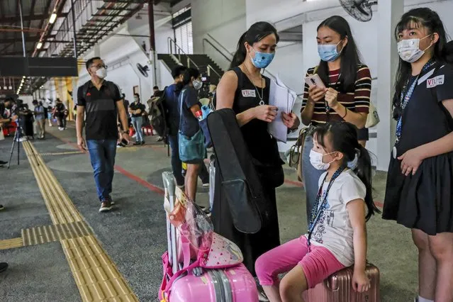 Chua Pei Sze, center, and her two daughters wait at the Woodlands temporary bus interchange before boarding a bus that will transport them to Malaysia from Singapore Monday, November 29, 2021. Malaysians working in Singapore held joyful reunions with their loved ones after returning to their homeland Monday following the partial reopening of a land border that has been shuttered for nearly two years due to the pandemic. (Photo by Toh Ee Ming/AP Photo)