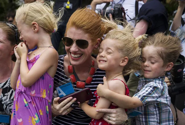 Karen Travers, ABC White House corespondent, second from left, holds her children, Maeve Anderson 6, left, Kelly Anderson 3, and Mathew Anderson 3, as they are buffeted by rotor wash from Marine One, with President Donald Trump aboard, on the South Lawn of the White House before departing, Wednesday, July 17, 2019, in Washington. (Photo by Alex Brandon/AP Photo)