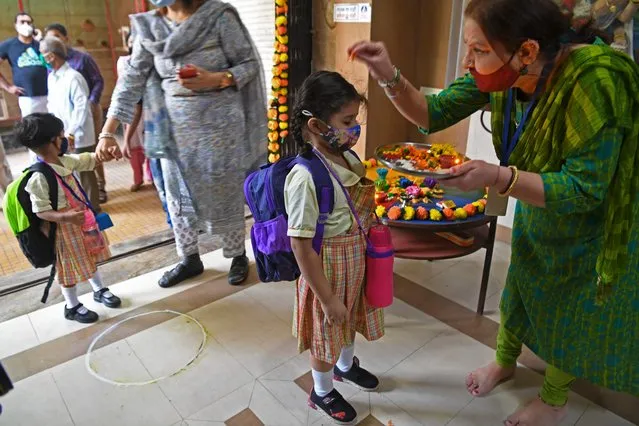 A teacher traditionally welcomes a student upon her arrival at a school in Mumbai on January 24, 2022, after schools were reopened that were closed as a preventive measure to curb the spread of the Covid-19 coronavirus. (Photo by Indranil Mukherjee/AFP Photo)