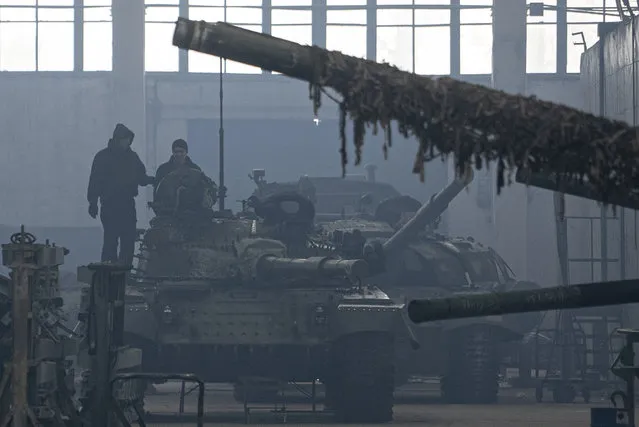 Workers stand atop a tank T-64 on Repair Tank Factory in Kharkiv, Ukraine, Monday, January 31, 2022. The situation in Kharkiv, just 40 kilometers (25 miles) from some of the tens of thousands of Russian troops massed at the border of Ukraine, feels particularly perilous. Ukraine's second-largest city is one of its industrial centers and includes two factories that restore old Soviet-era tanks or build new ones. (Photo by Evgeniy Maloletka/AP Photo)