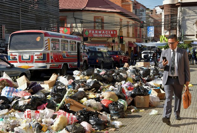 A man walks near garbage accumulated over several days in the streets since residents of the Tamborada neighbourhood have been blocking access to the K'ara K'ara landfill, due to a dispute over land prices with a local university, in Cochabamba, Bolivia on April 24, 2023. (Photo by Patricia Pinto/Reuters)