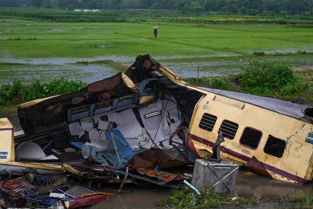 A villager walks past the wreckage of Kanchenjunga Express passenger train at Rangapani in India's West Bengal state on June 18, 2024. At least eight people were killed in India on June 17 when a goods train driver missed a signal and slammed into an express passenger train from behind, police and railway officials said. (Photo by Dibyangshu Sarkar/AFP Photo)