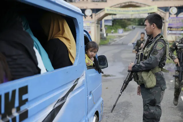 In this June 8, 2017 photo, a baby girl watches a soldier at a military checkpoint in Marawi city, southern Philippines. Trapped Filipinos are trickling out of Marawi city with harrowing tales of survival more than two weeks after Islamic militants plunged the southern Philippine city into chaos with an unprecedented attack. (Photo by Aaron Favila/AP Photo)