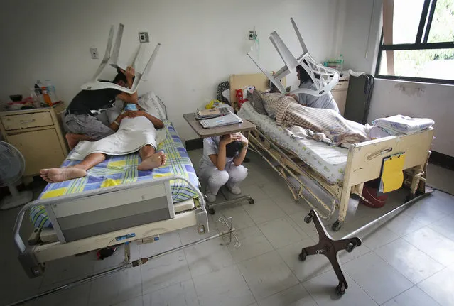 Caregivers of patients hold plastic chairs over their heads while a nurse takes cover under a table as they participate in a metropolitan Manila-wide earthquake drill designed to boost preparedness in the country at the Veterans Memorial Medical Center in suburban Quezon city, north of Manila, Philippines on Thursday, July 30, 2015. Filipinos poured out of buildings and shopping malls in a massive drill across Manila on Thursday to brace for an earthquake that experts fear could kill tens of thousands and displace millions. (Photo by Aaron Favila/AP Photo)