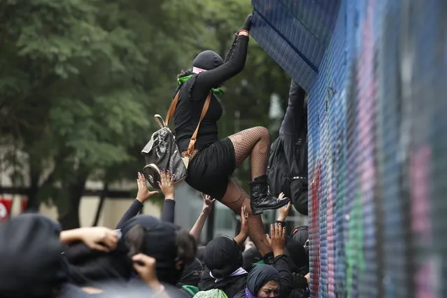 A woman climbs a barricade that protects the Angel of Independence monument, during an abortion-rights demonstrators on the Day for Decriminalization of Abortion in Latin America march, in Mexico City, Tuesday, September 28, 2021. (Photo by Ginnette Riquelme/AP Photo)
