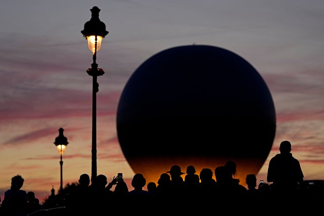 People wait for the balloon carrying the Olympic cauldron to rise above Tuileries Garden during the 2024 Summer Olympics, Tuesday, August 6, 2024, in Paris, France. (Photo by Charlie Riedel/AP Photo)