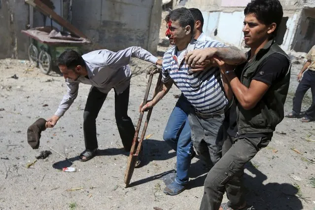Men help an injured civilian after what activists said were airstrikes by forces loyal to Syria's President Bashar al-Assad on a busy marketplace in the Douma neighborhood of Damascus, Syria August 12, 2015. (Photo by Bassam Khabieh/Reuters)
