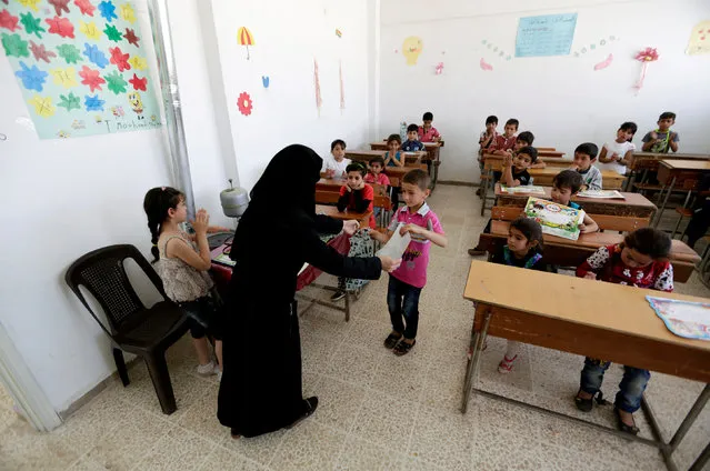Students receive certificates and gifts at the end of the school year, inside 'Syria, The Hope' school on the outskirts of the rebel-controlled area of Maaret al-Numan town, in Idlib province, Syria June 1, 2016. The school is partially occupied and it teaches students until fourth grade. The building that is heavily damaged was used by government forces as a base before the rebel fighters took control of the area. (Photo by Khalil Ashawi/Reuters)