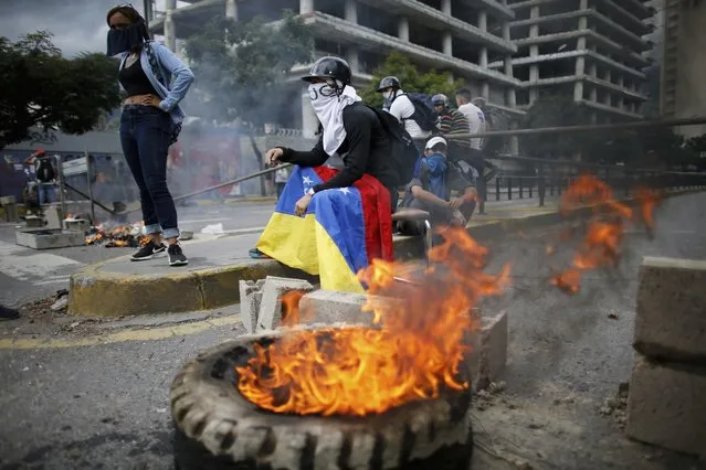 Masked anti-government demonstrators stend to a burning barricade during a protest against the installation of a constitutional assembly in Caracas, Venezuela, Friday, August 4, 2017. (Photo by Ariana Cubillos/AP Photo)