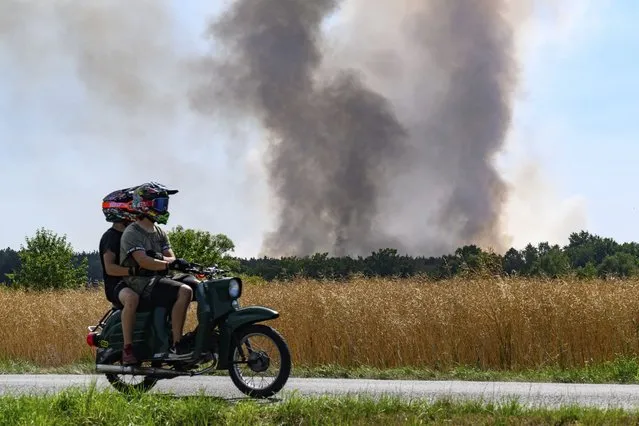 A couple on a moped look at a forest fire near Radeburg in Germany, Tuesday, July 19, 2022. The double blow of heat waves and droughts exacerbated by climate change are making wildfires more frequent, destructive and harder to fight. (Photo by Robert Michael/dpa via AP Photo)