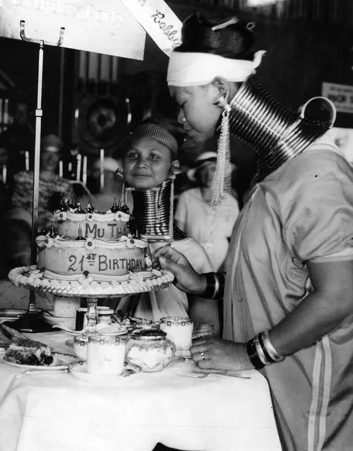 A Burmese woman, with traditional neck-extending rings, celebrates her twenty-first birthday with a cake in Folkestone with her friend. They are both part of Bertram Mills Circus, where they are billed as the “giraffe-necked Burmese ladies”. 25th August 1936. (Photo by A. J. O'Brien)