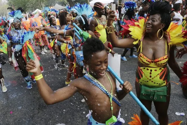 A young dancer laughs as he is showered with ice water during the West Indian Day Parade, Monday, September 1, 2014 in the Brooklyn borough of New York. (Photo by Mark Lennihan/AP Photo)