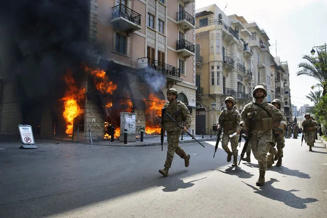 Lebanese army soldiers run in front of a Credit Libanais Bank that was set on fire by anti-government protesters, in the northern city of Tripoli, Lebanon, Tuesday, April 28, 2020. Hundreds of angry Lebanese took part Tuesday in the funeral of a young man killed in riots overnight in the northern city of Tripoli that were triggered by the crash of Lebanon's national currency that sent food prices soaring. (Photo by Bilal Hussein/AP Photo)