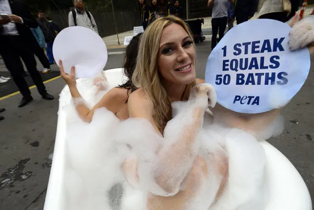A protester from the People for the Ethical Treatment of Animals (PETA) displays a placard from a bathtub as a people looks on during a demonstration to call on the public to eat more vegetables to save water, in Sao Paulo on August 2, 2016. (Photo by Cris Faga via ZUMA Wire)