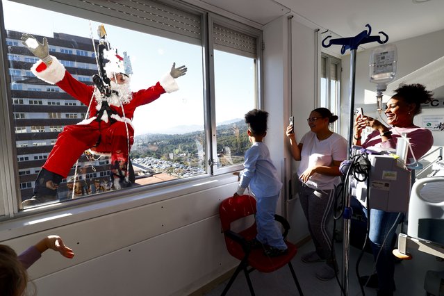 A man dressed in Santa Claus costume waves out of the window a girl as he visits Germans Trias Hospital in Badalona, Barcelona, Spain, 19 December 2023. Santa Claus arrived the hospital using a zipline. (Photo by Quique Garcia/EPA)