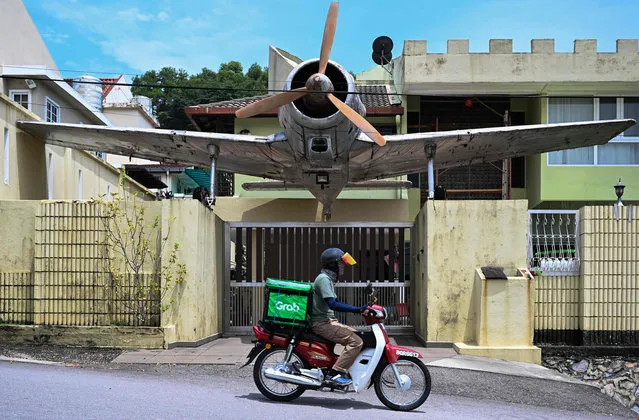A “Grab” delivery rider passes in front of a residence house decorated with a tourist aircraft, in Kuala Lumpur, on August 8, 2022. (Photo by Mohd Rasfan/AFP Photo)