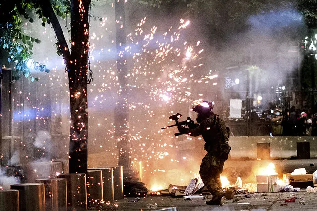 A federal officer fires crowd control munitions at Black Lives Matter protesters at the Mark O. Hatfield United States Courthouse on Friday, July 24, 2020, in Portland, Ore. Since federal officers arrived in downtown Portland in early July, violent protests have largely been limited to a two block radius from the courthouse. (Photo by Noah Berger/AP Photo)