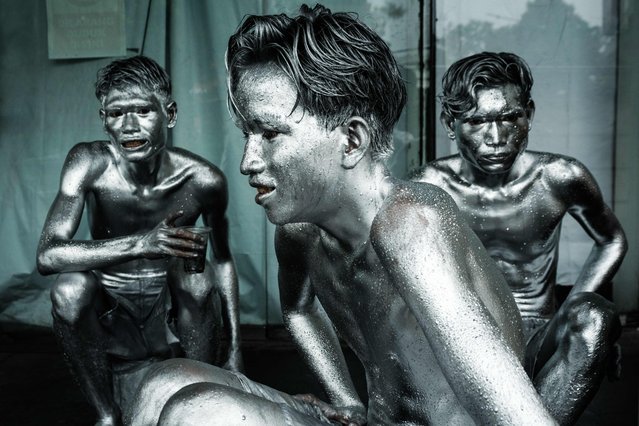 This photo taken on April 1, 2025 shows street performers Keris Munandar (L), his brother Ari Munandar (R), and their neighbour Riyan Ahmad Fazriyansah, taking shelter from the rain during their performance at an intersection in Jakarta. On a rainy day in Indonesia's capital Jakarta, three men coated in metallic paint known as the “manusia silver”, or silvermen, brave the elements at an intersection near a mall to ask drivers for change. (Photo by Yasuyoshi Chiba/AFP Photo)