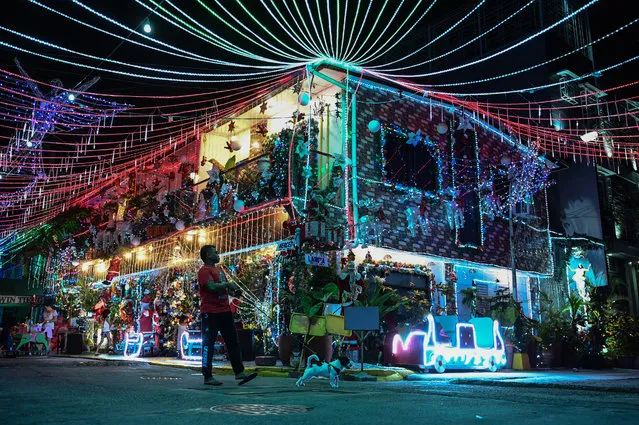 In this photo taken on December 21, 2022, a man walks with a dog past a Christmas-themed house in Manila. (Photo by Jam Sta Rosa/AFP Photo)