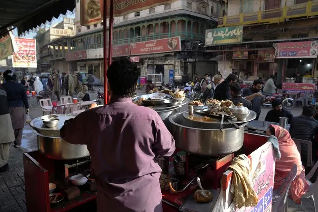 People eat breakfast at a famus food street of Gawalmandi, an old area of Lahore, Pakistan, Sunday, December 11, 2022. Gawalmandi is the city's neighborhood crammed with people, vehicles, animals, and food stalls. (Photo by K. M. Chaudary/AP Photo)