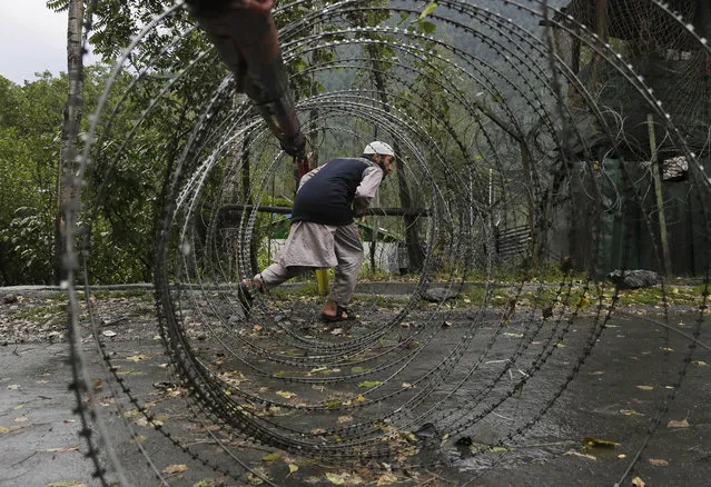 A Kashmiri man ducks to cross an iron barricade with coils of razor wire near a military base at Braripora, near the de facto border dividing Kashmir between India and Pakistan, in Indian controlled Kashmir, Wednesday, September 21, 2016. Indian soldiers on Wednesday searched areas near the de facto border where two gunbattles with suspected rebels raged for half a day, the Indian army said. The clashes came three days after suspected rebels killed more than 15 Indian soldiers in an audacious attack on a crucial military base in Uri. The militants also were killed. (Photo by Mukhtar Khan/AP Photo)