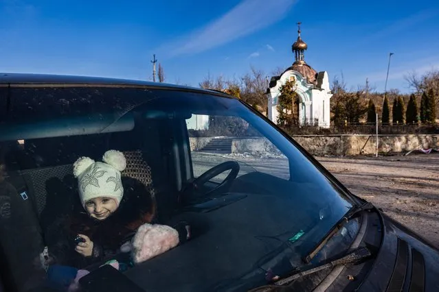 A girl smiles at a car in the destroyed village of Bohorodychne, eastern Ukraine on December 20, 2022. Bohorodychne is a village in Donetsk region that came under heavy attack by Russian forces in June 2022, during the Russian invasion of Ukraine. On August 17, 2022 the Russian forces captured the village. The Armed Forces of Ukraine announced on September 12, 2022 that they took back the control over the village. A few resident came back to restore their destroyed houses and live in the village. (Photo by Sameer Al-Doumy/AFP Photo)