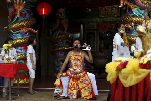 A devotee of the Chinese Bang Neow shrine sits with an axe pierced through his cheek during a procession celebrating the annual vegetarian festival in Phuket, Thailand October 18, 2015. (Photo by Jorge Silva/Reuters)