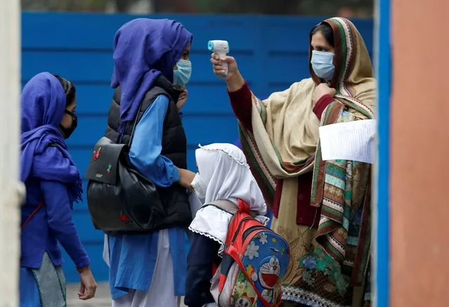 A teacher checks body temperatures of students as they arrive at a school in Lahore, Pakistan, Wednesday, November 25, 2020. Pakistan will again close all educational institutions as of Thursday Nov. 26, 2020, because of a steady and increasingly drastic increase in coronavirus cases. (Photo by K.M.Chaudary/AP Photo)