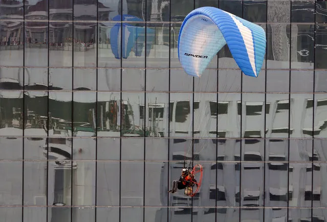 A pilot guides his powered paraglider between buildings while flying in central Jakarta, Indonesia September 25, 2016. (Photo by Darren Whiteside/Reuters)