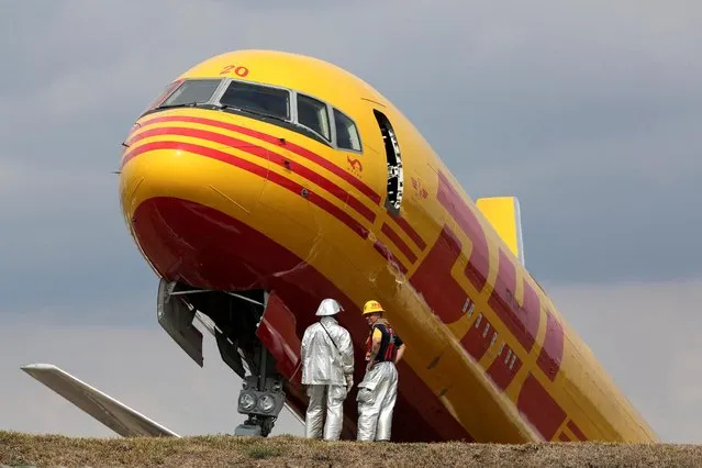 Firefighters stand at the scene where a Boeing 757-200 cargo aircraft operated by DHL made an emergency landing before skidding off the runway and splitting, aviation authorities said, at the Juan Santamaria International Airport in Alajuela, Costa Rica on April 7, 2022. (Photo by Mayela Lopez/Reuters)
