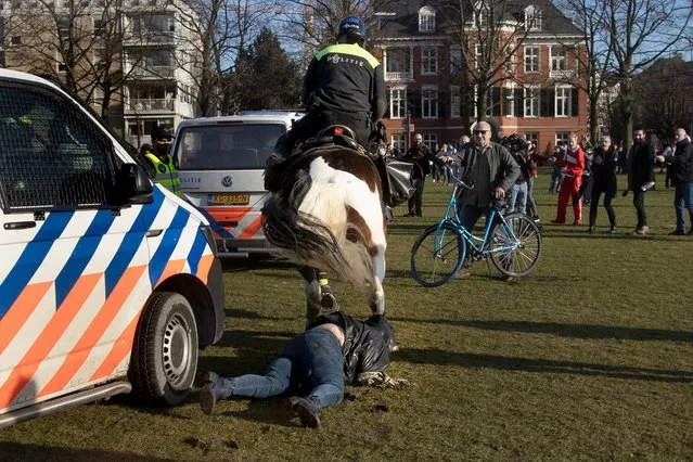 A woman gets trampled by a police horse during a demonstration of several hundreds of people protesting against the coronavirus lockdown and curfew in Amsterdam, Netherlands, Sunday, February 21, 2021. (Photo by Peter Dejong/AP Photo)