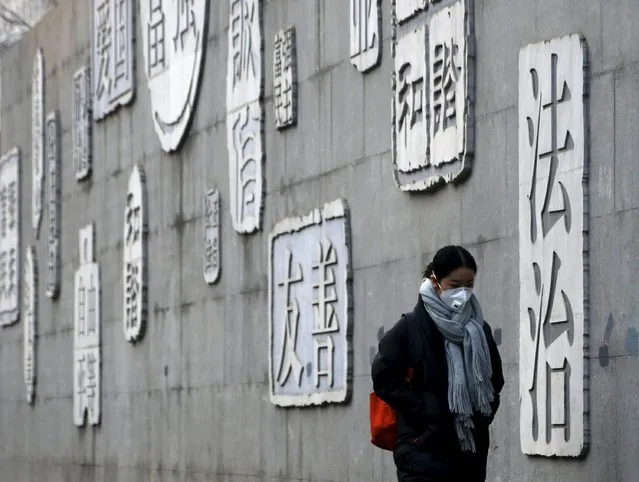 A woman wearing a protective mask walks past a wall of a school bearing educational slogans in Beijing, China January 3, 2016. (Photo by Kim Kyung-Hoon/Reuters)