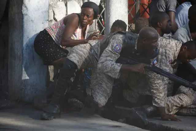 A woman takes cover between Haitian National Police officers during clashes after a ceremony for the anniversary of the killing of Jean-Jacques Dessalines in Port-au-Prince, Haiti, October 17, 2018, Haiti on October 17, 2018. (Photo by Andres Martinez Casares/Reuters)