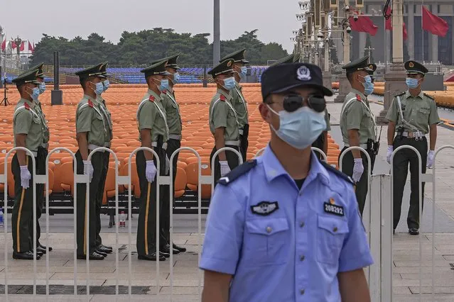 A police officer wearing a face mask to help curb the spread of the coronavirus stands guard near masked Chinese paramilitary officers preparing for their duties near rows of seats setup on Tiananmen Square in Beijing, Monday, June 28, 2021. China is marking the centenary of its ruling Communist Party this week by heralding what it says is its growing influence abroad, along with success in battling corruption at home. (Photo by Andy Wong/AP Photo)
