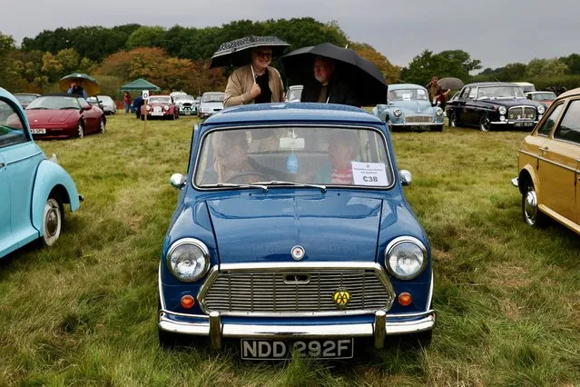 Malcolm Jacques and Clive Barber stand with a Morris Mini mk2 car from 1968 as their wives Carol and Judith shelter from the rain inside, at the Pistons and Paws classic car show in Tenterden, Britain on September 17, 2023. (Photo by Kevin Coombs/Reuters)