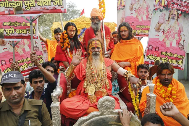 Indian godman Golden Baba, known for the gold ornaments he wears gestures as Hindu holy men arrive in a procession ahead of the Kumbh Mela in Allahabad, India, Wednesday, November 28, 2018. Millions of Hindu pilgrims are expected to take part in the large religious congregation scheduled to be held in January 2019 on the banks of rivers the Ganges and the Yamuna. Placards in Hindi read, “Golden Puri Baba Ji”. (Photo by Rajesh Kumar Singh/AP Photo)