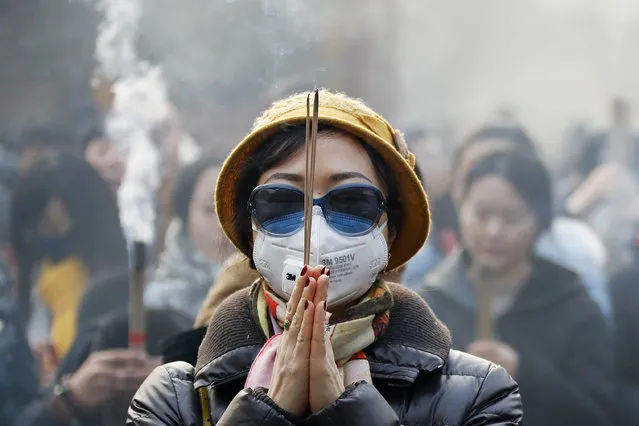 A Chinese woman wearing a mask and a pair of sunglasses prays while holding burning joss sticks on the first day of the New Year at Yonghegong Lama Temple in Beijing, on a heavily polluted day, Sunday, January 1, 2017. (Photo by Andy Wong/AP Photo)
