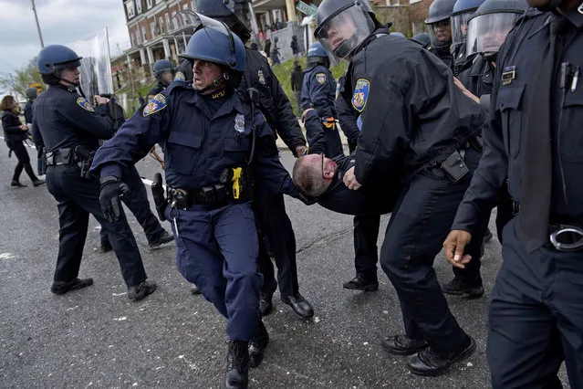 Baltimore police officers carry an injured comrade as they clash with protesters in the streets near Mondawmin Mall April 27, 2015 in Baltimore, Maryland. Violent street clashes erupted in Baltimore on Monday after friends and family gathered for the funeral of Freddie Gray, a 25-year-old black man whose death in custody triggered a fresh wave of protests over US police tactics. (Photo by Brendan Smialowski/AFP Photo)