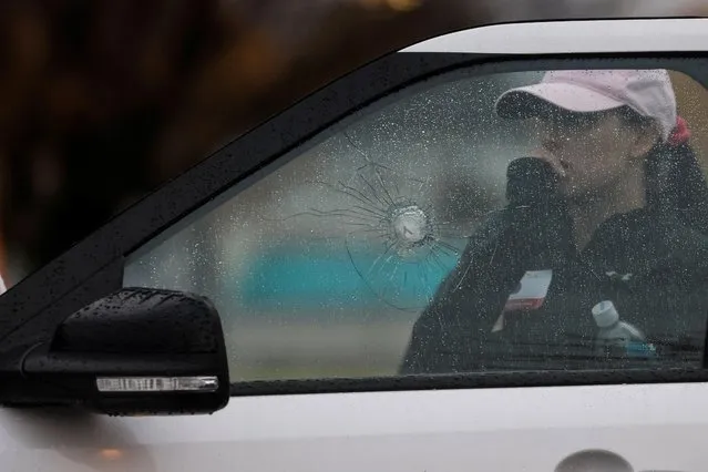 A woman stands behind a car with shattered glass near the scene of a shooting at the Boise Towne Square shopping mall in Boise, Idaho, U.S., October 25, 2021. Two people were killed and four others, including a police officer, were injured in a shooting at the shopping center. (Photo by Shannon Stapleton/Reuters)