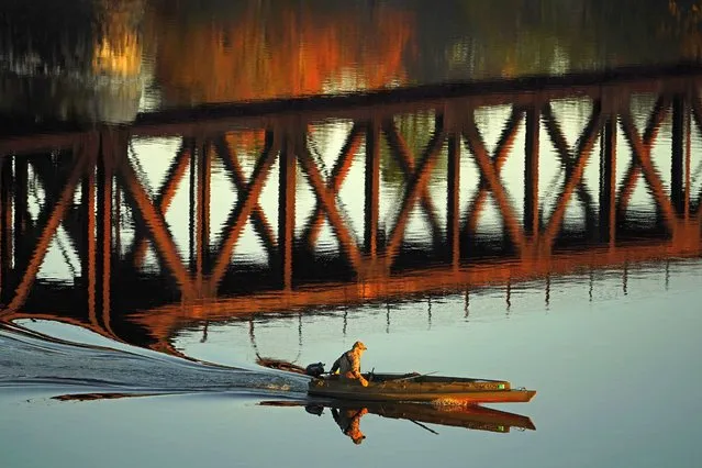 A duck hunter motors by the reflection of a train trestle on the Androscoggin River, Friday, October 29, 2021, in Brunswick, Maine. (Photo by Robert F. Bukaty/AP Photo)