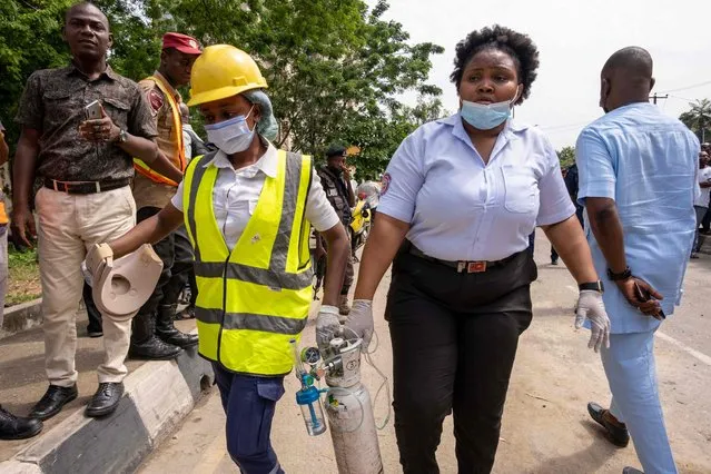 Rescue workers carry an oxygen tank towards the site of the collapsed 21-storey building in Ikoyi, Lagos, on November 2, 2021. (Photo by Benson Ibeabuchi/AFP Photo)