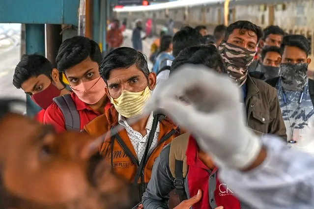 Passengers queue up as they watch a nasal swab sample being taken during a Covid-19 coronavirus screening after arriving at a railway platform on a long distance train, in Mumbai on January 7, 2022. (Photo by Punit Paranjpe/AFP Photo)